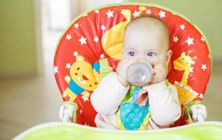 baby drinking from bottle sitting in high chair photo