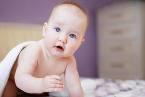 lindo bebé mirando a la cámara bajo una toalla blanca. retrato de un niño lindo foto