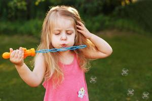 Cute little girl is blowing soap bubbles photo