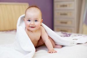 lindo bebé sonriente mirando a la cámara bajo una toalla blanca. retrato de un niño lindo foto