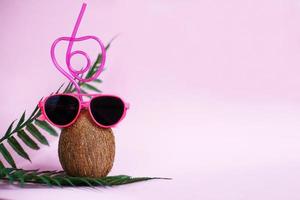 A coconut with straw and pink sunglasses on pink background. Summer and trave concept. copy space photo