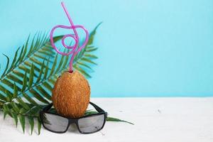 A coconut with straw and black sunglasses on blue background. Summer and trave concept. copy space photo