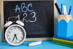 libros de texto y despertador con pizarra escolar sobre un fondo azul. De vuelta a la escuela. concepto de educación o negocios foto