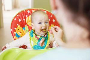 Mom feeds funny baby from a spoon . child eats in a highchair photo