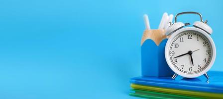 Textbooks and alarm clock on a blue background. Back to school. Concept Education or business. banner photo