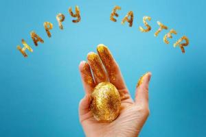 Easter golden egg in the hand on a blue background. Easter background. hand and egg in gold sparkles. happy Easter photo