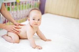 Mother massaging baby in bed at home photo