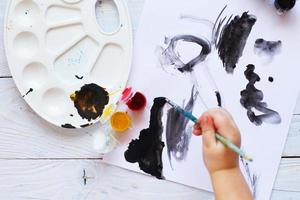 view from above. child draws a brush and paints top view. Flat lay art tools for painting.Artwork workplace photo