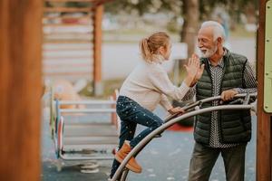 Grandfather spending time with his granddaughter in park playground on autumn day