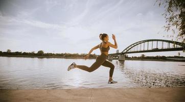 hermosa mujer joven activa corriendo en el paseo marítimo a lo largo de la orilla del río foto