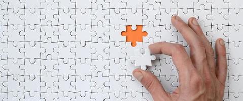 The texture of a white jigsaw puzzle in the assembled state with one missing element that the male hand puts in photo