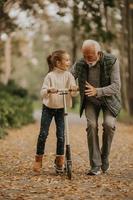 un anciano enseñando a su nieta a andar en patinete en el parque foto