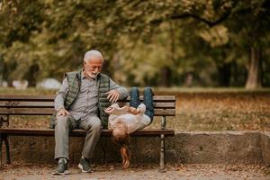 Grandfather spending time with his granddaughter on bench in park on autumn day photo