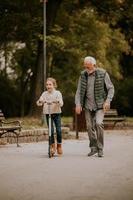 un anciano enseñando a su nieta a andar en patinete en el parque foto