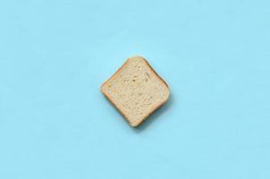 A piece of bread lies on texture background of fashion pastel blue color paper in minimal concept photo