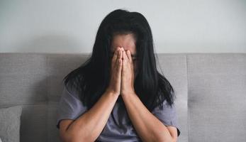 Schizophrenia with lonely and sad in mental health depression concept. Depressed woman sitting against on the sofa at home with dark room feeling miserable. Women are depressed, fearful and unhappy. photo