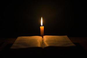 velas encendidas con la sagrada biblia y la cruz o el crucifijo sobre un fondo de madera antiguo en la iglesia. luz de las velas y libro abierto sobre una mesa de madera vintage estudio y lectura del cristianismo en el hogar. concepto de la religión de cristo foto