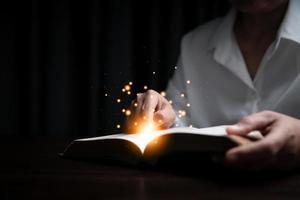Faith with holy bible concept. Hands of a female prayer worship God with holy bible on black background in church. Christian woman who believe in Jesus read and study the grace of the holy scriptures.