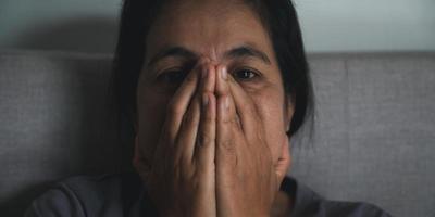 Schizophrenia with lonely and sad in mental health depression concept. Depressed woman sitting against on the sofa at home with dark room feeling miserable. Women are depressed, fearful and unhappy. photo