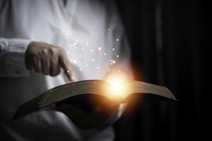 Faith with holy bible concept. Hands of a female prayer worship God with holy bible on black background in church. Christian woman who believe in Jesus read and study the grace of the holy scriptures. photo