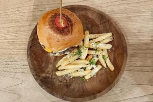 Burger with a stick and fried potato in a wooden plate serve on the table. photo