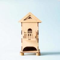 Miniature wooden toy house stands on gold coins. House foundation made of coins. Real estate cost concept, rental housing, construction business photo