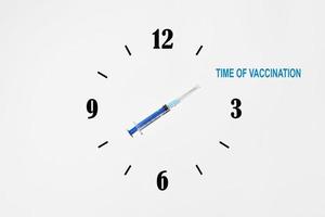 concepto creativo de vacunación de la población mundial. Jeringa que indica el tiempo de vacunación en la esfera del reloj foto
