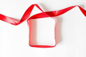 Red packing ribbon lying on white background in the shape of a gift box. Flat lay, copy space photo