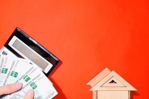 Man's hands counting money, calculator and a toy house. Red background top view, place for text. Calculation of personal finances, payment of utilities photo