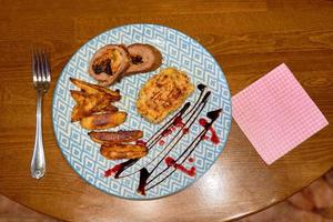 A beautifully presented dish of fried meat and baked potatoes in a plate that sits on the dining table. photo