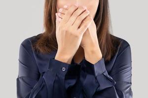 la mujer con una camisa azul oscuro no comenta y se niega. mujer con las manos en la boca por mal aliento o halitosis foto