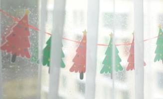 Decorated window with handmade paper garland of red and green Christmas trees.Festive mood. Christmas concept, holiday preparation.Happy New Year.Selective focus photo