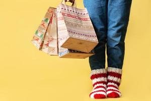 Delivery Christmas gifts shopping craft paper bags presents and child in knitted socks isolated yellow background photo