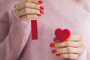 close up woman's hands with red manicure holds heart under wool pastel pink knitted sweater background I love you symbol Valentine's day photo