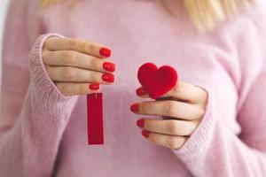 close up woman's hands with red manicure holds heart under wool pastel pink knitted sweater background I love you symbol Valentine's day photo