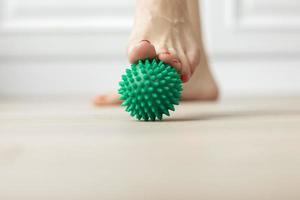 Woman doing flatfoot correction gymnastic exercise using massage ball at home Myofascial relaxation topic of preventing foot fatigue after wearing high-heeled shoes antistress ball photo