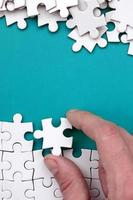 The hand folds a white jigsaw puzzle and a pile of uncombed puzzle pieces lies against the background of the blue surface. Texture photo with space for text