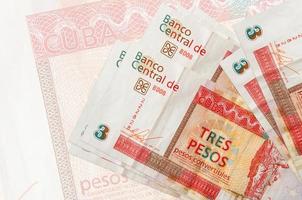 Los billetes convertibles de 3 pesos cubanos se encuentran apilados sobre el fondo de un gran billete semitransparente. presentación abstracta de la moneda nacional foto