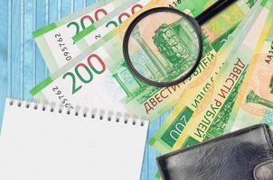 200 russian rubles bills and magnifying glass with black purse and notepad. Concept of counterfeit money. Search for differences in details on money bills to detect fake photo