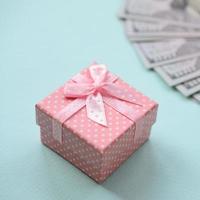 Pink dotted gift box lies near hundred dollar bills on a light blue background photo