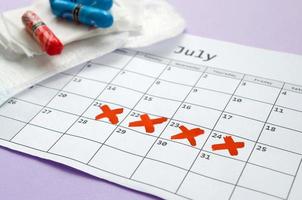 Menstrual pads and tampons on menstruation period calendar with red cross marks lies on lilac background photo