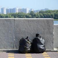 dos bolsas de basura negras en el suelo de la calle en una valla de hormigón en la ciudad foto