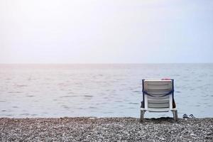 Chair on bank of pebbles with the sea and beach photo