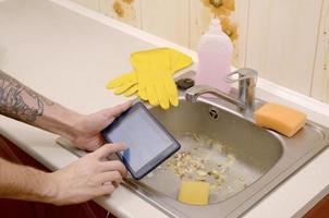 The landlord uses the tablet to call a cleaner in order to clean the clogged kitchen sink photo