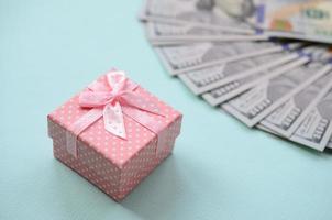 Pink dotted gift box lies near hundred dollar bills on a light blue background photo