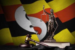 bandera de uganda con estatua de la dama de la justicia, constitución y martillo de juez sobre cortinas negras. concepto de juicio y culpa foto