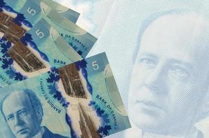 Los billetes de 5 dólares canadienses se encuentran apilados en el fondo de un gran billete semitransparente. fondo de negocios abstracto foto