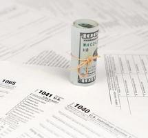 Tax forms lies near roll of hundred dollar bills. Income tax return photo