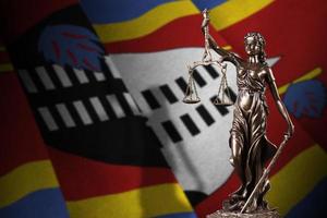 bandera de swazilandia con estatua de la dama de la justicia y escalas judiciales en cuarto oscuro. concepto de juicio y castigo foto
