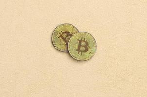 Two golden bitcoins lies on a blanket made of soft and fluffy light orange fleece fabric. Physical visualization of virtual crypto currency photo